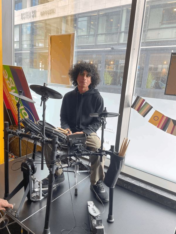 Arjun seated at an electronic drum kit near a window
